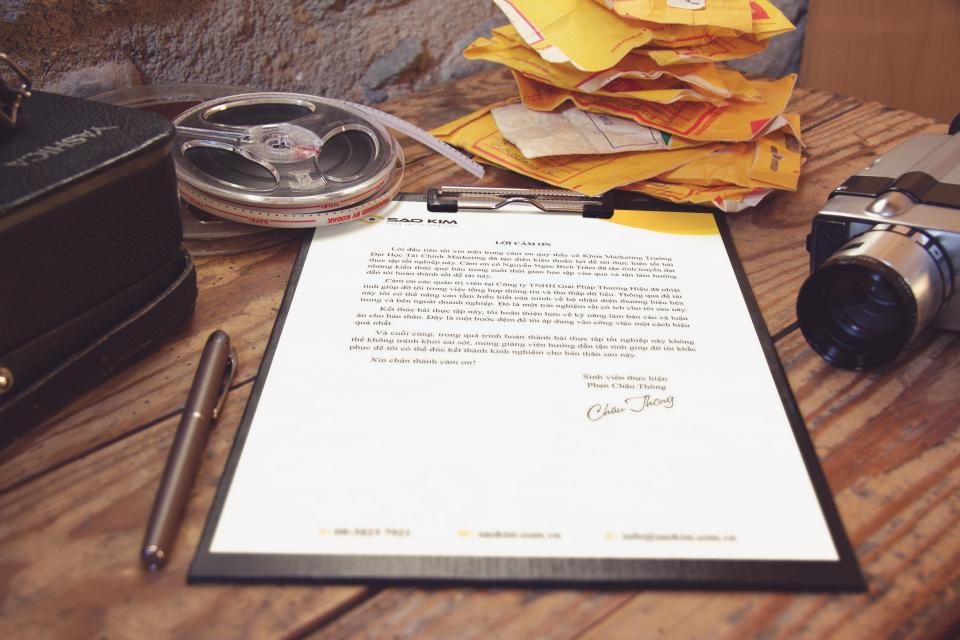 Contrato preso a uma prancheta sobre uma mesa de madeira, com uma caneta e uma câmera ao lado