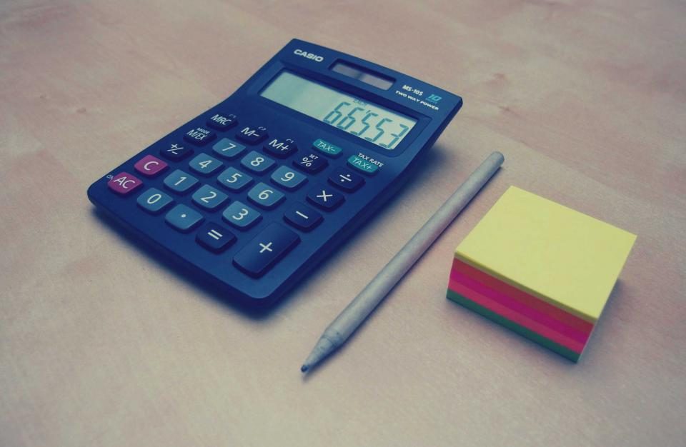 Calculadora azul sobre uma mesa, ao lado de um lápis e de blocos de notas coloridos