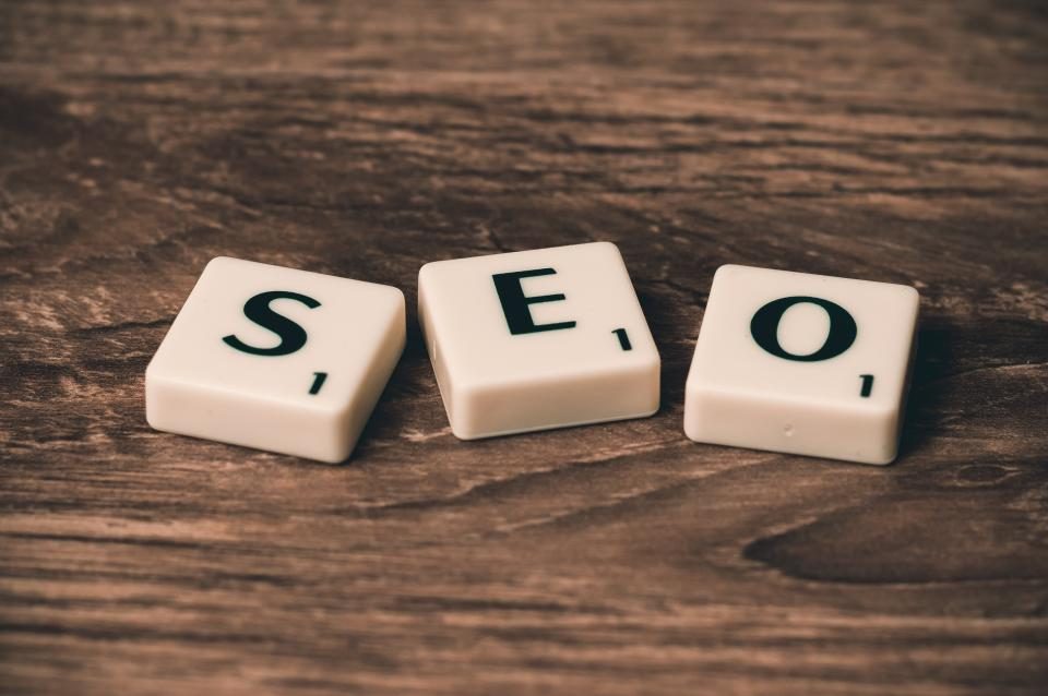 Peças de um jogo de palavras formando a sigla SEO sobre uma mesa de madeira